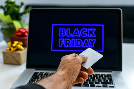 Hand with credit card in front of the laptop monitor doing purchases in an on line shop the black...
