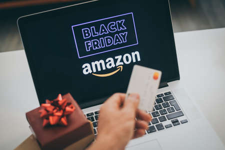 Hand with credit card in front of the laptop monitor doing purchases Amazon on line shop black friday. Purchase Christmas gifts. E-commerce, tech, online shopping concept Milan, Italy - November 2021のeditorial素材