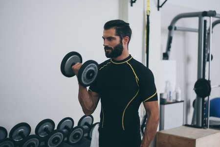 Determined young man working out in the gym. Fit male doing exercise with weights for biceps....
