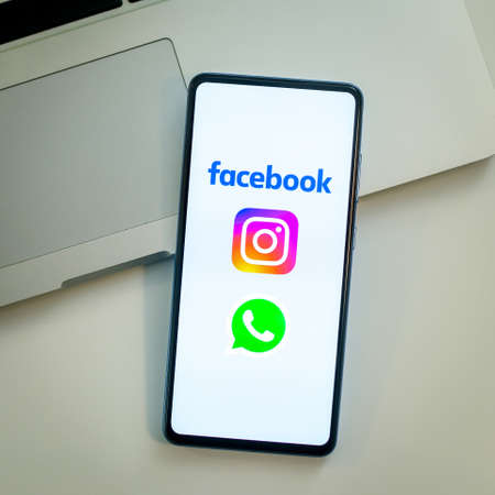 Close up view of a smartphone and Instagram, Facebook and Whatsapp logos on display. Laptop on...