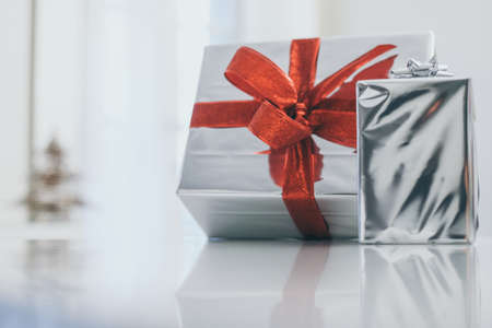 Gift boxes near Christmas tree inside home. Box with holiday ribbon with bows. Warm festive family...