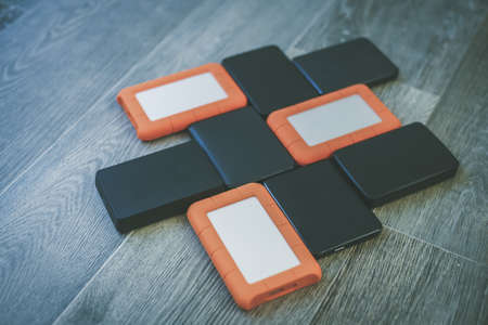 Many portable hard drives on the wooden floor. Mosaic of usb storage devices. External computer equipment. Cloud technology, online disk, remote backup, security copy and archiving Internet concept.の写真素材