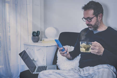 Man works with laptop sitting on the sofa. Male home working with remote office. Boy sitting in...