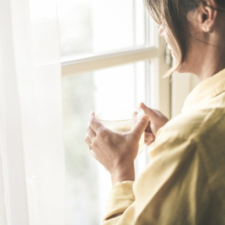 Young woman drinking a cup of tea looking outside the window Portrait of a girl enjoying free time at home. Middle aged female with a drink in the hand look through the door. Lifestyle leisure conceptの写真素材