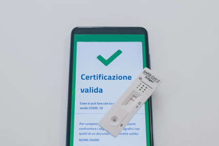Closeup view of gloved hand with SARS-CoV-2 rapid antigen test nasal and phone with green digital...