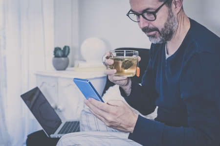 Man works with laptop sitting on the sofa. Male home working with remote office. Boy sitting in livingroom use online devices. Smart working, home school lifestyle new communication technology conceptの写真素材