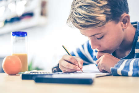 Student drawing with pencil on the notebook. Boy doing homework writing on a paper. Kid hold a pencil and draw a manga at home. Teen drawing sitting at the table. Education art talent ability concept.の写真素材