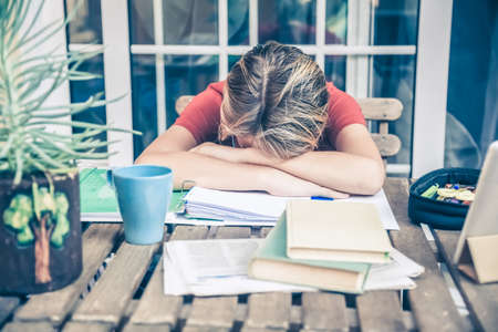 Tired student doing homework at home sitting outdoor with school books and newspaper. Boy weary due to heavy study. Kid asleep on the copybook after long tasks. Youth, education and fatigue concept.の写真素材