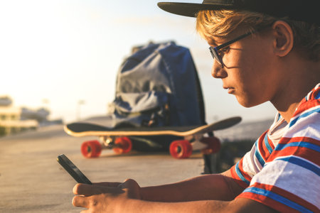 Portrait of a beautiful teen using smartphone social app leaning on a concrete wall outdoor. Young trendy boy watching social video online on cellphone Youth urban lifestyle and new technology conceptの写真素材