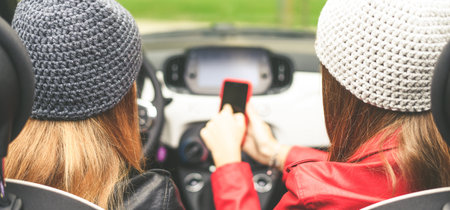 Trendy girls sitting in the car. Teen in front of the steering wheel with a friend using smartphone beside. Young fashion women enjoying free time in a convertible car. Youth, freedom, travel concept.の写真素材