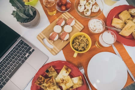 View from the top of a table with many foods ready for an aperitif with family and friends. Dinner at home with fresh finger food, tapas, beer and laptop computer. Meal, party, togetherness conceptの写真素材