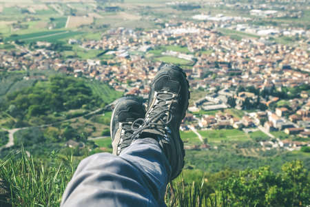 Trekking shoes and mountain panorama. Male legs and feet with technical hiking boots. Relax on the top enjoying landscape. Freedom, outdoors, lifestyle, travel, concept. Montecatini Monsummano Termeの写真素材