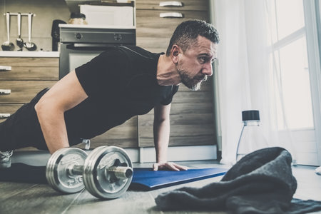 Determined sporty young man working out and trains at home. Fit boy doing push-ups exercises on the mat. Strong boy do gymnastics in the living room. Wellness, health, sport, gym, training conceptの写真素材