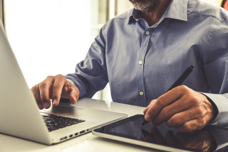 Closeup man hands using laptop and tablet. Businessman works with computer and digital pad at homeの写真素材