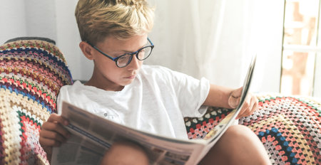 Young boy reading a newspaper at home. Child reads news. Information culture and educational conceptの写真素材