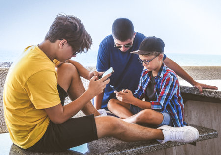 Teenagers friends using smartphones together. Smiling teens browsing social media online. Boys watching video streaming on mobile phone. Youth, technology, generation z lifestyle communication conceptの写真素材