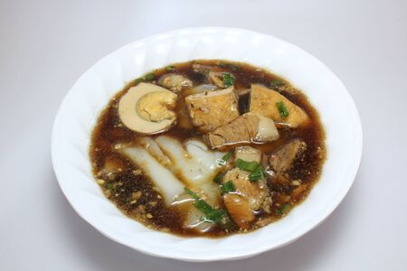 Chinese roll noodle soup (Guay Jub Nam Kon call in Thai) with crunchy pork, egg and cinnamon in white bowl on white background, itâs one of the top Thai street food dishes to tryの写真素材