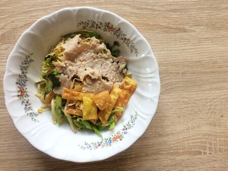 Dried egg noodles in a bowl mix topping with chopped pork, onion and fried wonton sheet, top viewの写真素材