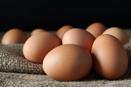 Fresh chicken eggs on burlap sack with black background, concept for homemade organic food.