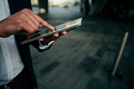 Mixed race business man typing on digital tablet scrolling while standing outside work officeの写真素材