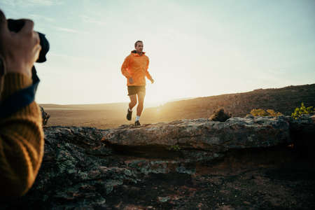 Photo shoot of Caucasian male student hiking in mountain running on path enjoying exercise while sun sets in horizonの写真素材
