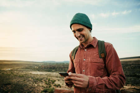 Caucasian male photographer walking through wilderness typing in cellular device posting to social...