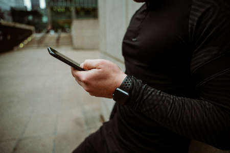 Caucasian male athlete scrolling on smartphone checking activity update while on outdoor runの写真素材
