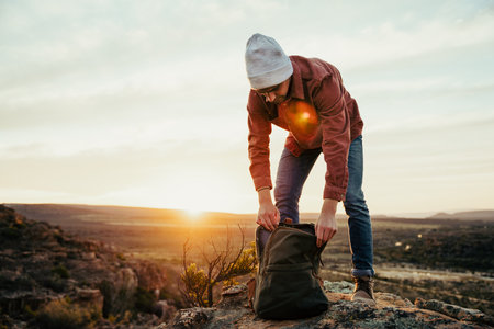 Caucasian male free spirit walking through wilderness at sunrise unpacking water from backpack