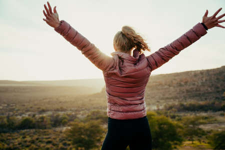 Caucasian female athlete hiking on mountain raising arms admiring sunset