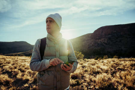 Caucasian male walking through mountain path using smartphone to locate directions on hiking trailの写真素材