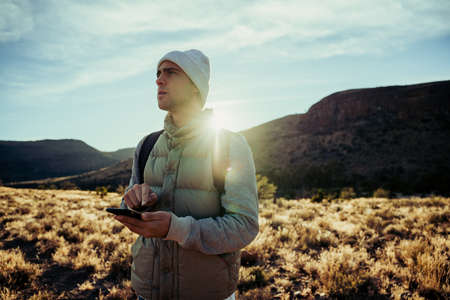 Single male athlete doing exercise hiking through mountain path messaging girlfriend with smartphone