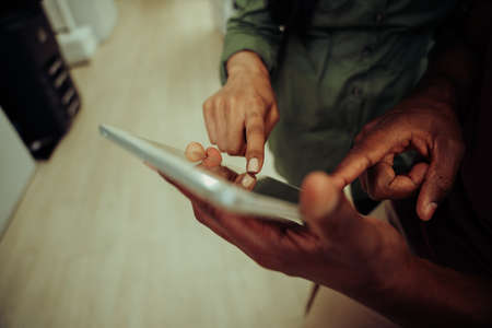 Close up of multi-ethnic co-workers working on collaboration project typing on digital tabletの写真素材