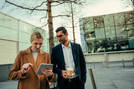 Mixed race business partners discussing ideas wile researching on digital tablet walking to workの写真素材