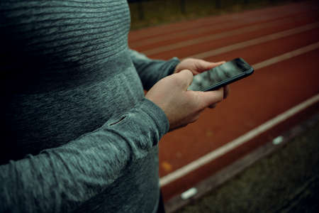 Close up caucasian male athlete typing on cellular device standing on tracking fieldの写真素材