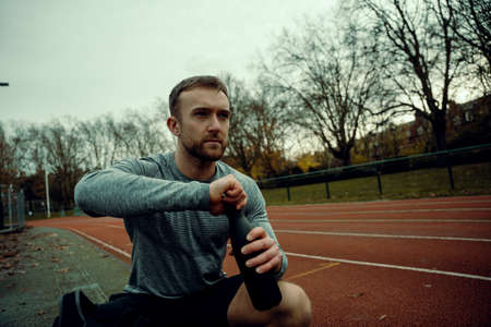 Caucasian male athlete sitting on tracking field opening water bottleの写真素材