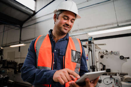 close up of caucasian engineer scrolling on digital tablet researching techniques while standing in factoryの写真素材
