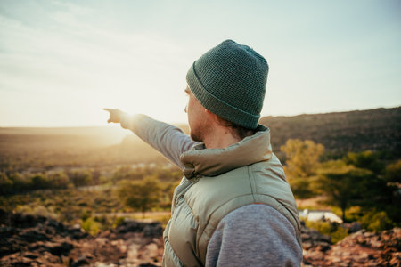 Caucasian male free spirit pointing at sunset in distance while walking in wildernessの写真素材