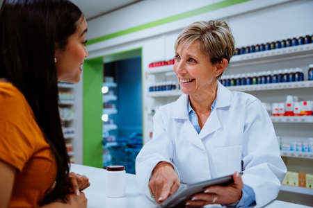 Senior pharmacist explaining medication guide to mixed race client standing in pharmacyの写真素材
