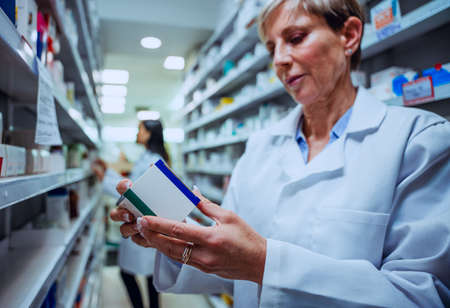 Caucasian elderly pharmacist looking at prescriptions medication labels on boxes for customersの写真素材