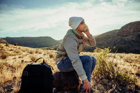 Young caucasian teenager chatting to friends while spending alone time hiking in mountain terrain