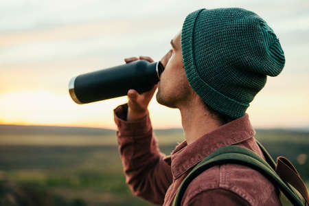 Caucasian male adventurer wearing beanie hiking in mountain quenching thirst drinking water