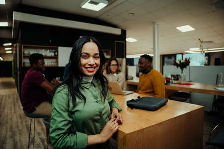 Portrait of Indian business woman smiling taking lunch break while colleagues prepare for meeting...