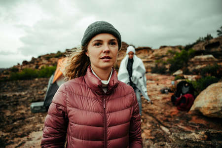 Caucasian female wearing beanie looking into distance camping on top of mountain with partner, romantic adventureの写真素材