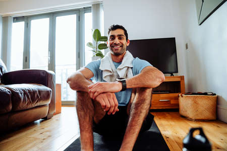 Mixed race male exercising in home sitting on floor with sweat towel smiling