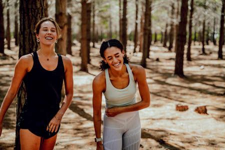 Two female friends laughing together standing in forestの写真素材