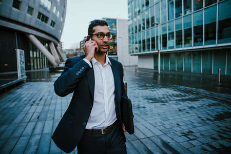 Mixed race businessman talking on cellular device while rushing walking to meeting in office block