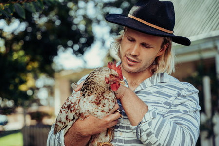 Caucasian male father petting pet chicken standing in farm village holding animal in handの写真素材