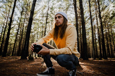 Handsome young caucasian male photographer in the woods taking photos and enjoying hobbyの写真素材