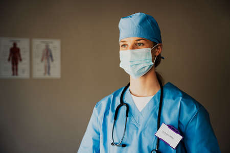 Caucasian female nurse wearing scrubs prepared to see symptomatic patient in doctors clinicの写真素材