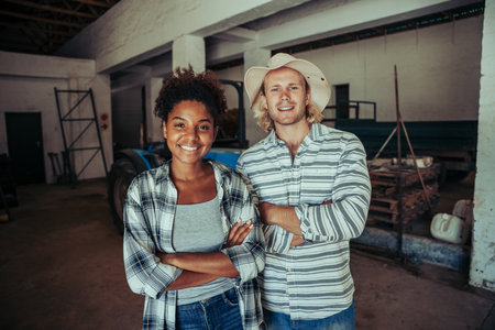 Mixed race farmers standing with crossed arms smiling in farm stableの写真素材